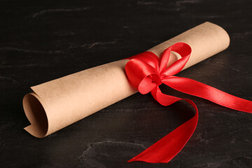 Rolled student's diploma with red ribbon on black table