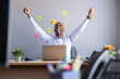 © Westend61 - Cheerful businessman with arms raised while sitting with laptop at office