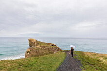 New Zealand, Oceania, South Island, Otago, Dunedin, Rear View Of Woman With Umbrella On Footpath NearTunnel Beach