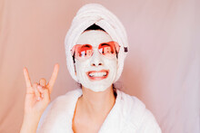 Happy Young Woman With Beauty Face Mask Showing Horn Sign Against Peach Background