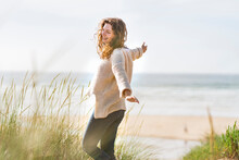 Carefree Woman With Arms Outstretched Standing Amidst Dunes At Beach