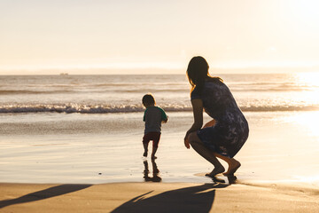 Woman Crouching Behind Son Running On Shore