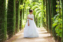 Girl In White Communion Dress Looking Down While Standing In Garden