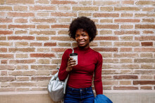 Smiling Young Woman With Reusable Cup Standing In Front Of Brick Wall
