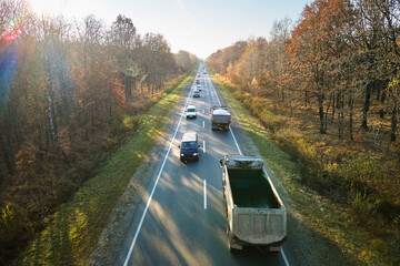 Canvas Print - Aerial view of intercity road with fast driving cars between autumn forest trees at sunset. Top view from drone of highway traffic in evening