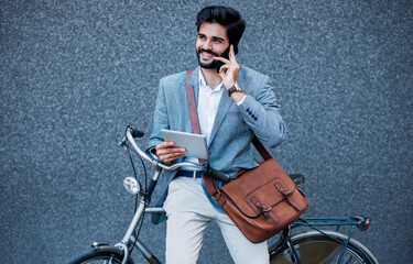 Wall Mural - Businessman holding tablet and making a phone call in front of the corporation. Business, lifestyle concept