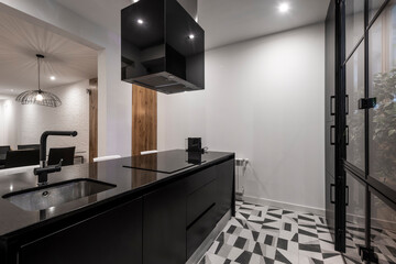 island and kitchen cabinet with black appliances next to a window with plants in a vacation rental apartment