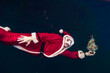 freediver dressed as Santa Claus swims underwater with a Christmas tree in his hand. Merry Christmas greetings from under the water. Underwater Santa. Santa is diving. Extreme sports and recovery