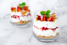 Strawberry dessert with cream cheese or yogurt, granola and fresh strawberry in glass on marble background. Recipe of simple layered dessert with fresh berry and jam. Lactose free vegan dessert.