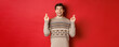Image of excited and hopeful young man making wish, wearing winter sweater, crossing fingers for good luck and smiling, anticipating christmas eve, standing over red background