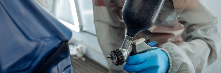 Banner . automobile repairman painter hand in protective glove with airbrush pulverizer painting car body in paint chamber.