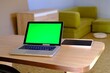 © Mariya_Maerdon - Silver laptop computer with chromakey green display and tablet in the room behind a robot vacuum cleaner and a wooden chest of drawers and a green sofa . High quality photo