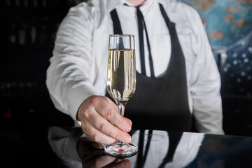 A professional bartender serves chilled champagne sparkling with gases in glass on the bar