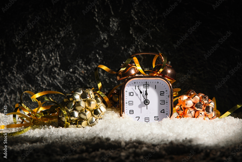 Golden alarm clock and Christmas decorations on snow against dark background