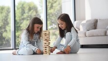 Wooden Construction Falls Down. Plays Tower Game. Two Cute Little Girls In Nightwear Together At Daytime In Modern Room