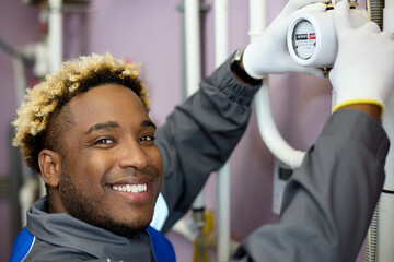 Smiling African-American worker in overalls takes the meter readings. Close-up of a black man in white gloves engaged in maintenance of equipment in a boiler room