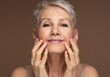 Portrait of gorgeous happy mature woman, senior older 60 year lady looking at camera touching her face