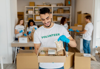 Wall Mural - Millennial male volunteer working at charity center, holding food donation box, proud of working at charity center