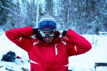 Caucasian woman in winter forest. Girl enjoys the snow falls. Close up portrait of snowboarder woman at ski resort wearing goggles with reflection of forest in mountains. 