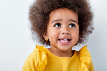 Cheerful little african girl isolated on white studio background, having fun, looks up, copyspace for ad. Looks happy, cheerful, sincere. Childhood, human emotions, facial expression concept.