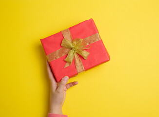 Wall Mural - female hand holding red gift box on a yellow background, concept of congratulations