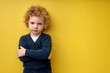 © alfa27 - Offended sad child boy stand with arms folded posing isolated on yellow studio background. Portrait of caucasian kid with curly hair sulking and pouting expressing kid anger, copy space