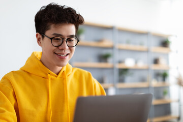 Smiling asian man working on laptop at home