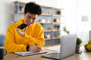 Wall Mural - Asian guy using voice assistant on cellphone