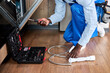 © alfa27 - Cropped Professional Handyman Of African American Appearance In Blue Overalls Repairing Dishwasher, Using Instruments Opening Toolbox, In Kitchen Floor At Home. Close-up hands