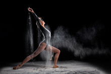 Flexible Ballet Dancer Woman Dancing And Sprinkle Flour On Black Background, Attractive Slim Slender Lady In Black Bodysuit In Slow Motion, Moving Gracefully. Full-length Portrait, Side View