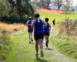 © coachwood - Rear view of boys running in a cross country race on a grass field