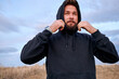 © alfa27 - Handsome guy wearing hoodie hood, preparing for sport, training outdoors, looking at side in contemplation. young male. european male in black wear outfit is engaged in healthy lifestyle