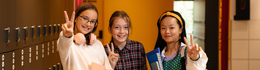 Multiracial girls showing peace sign and smiling together at school