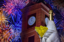 Glass With Grapes On The Background Of A Blurry Bottle Of Champagne, Clock Tower In Twelve O'clock And Fireworks. Spanish Tradition Of Eating Twelve Grapes To Celebrate New Year.