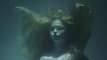 Close-up Of A Beautiful Girl With Red Hair In A White Dress Froze Under Water