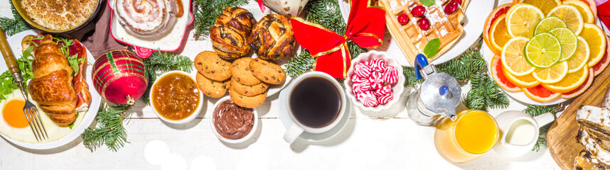 Festive Christmas morning breakfast or brunch table, with traditional foods – pancakes, Belgian waffles, fried eggs, croissant, stolen, cookies, with orange juice and coffee, cinnamon rice porridge 