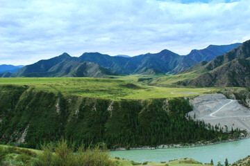 Wall Mural - The very high bank of the Katun River is covered with a forest, on the right there is a road, at the top there is a large green meadow, in the distance there are mountain ranges with rocky slopes, sum