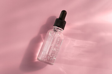 Transparent glass dropper bottle with air bubbles on pink background in sunlight. Pipette with fluid hyaluronic acid, serum, retinol. Cosmetics and healthcare concept Flat lay. Luxury beauty product