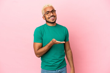 Wall Mural - Young Colombian handsome man isolated on pink background presenting an idea while looking smiling towards