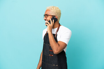 Sticker - Restaurant Colombian waiter man isolated on blue background keeping a conversation with the mobile phone with someone