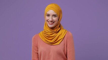 Wall Mural - Smiling young arabian asian muslim woman in abaya hijab yellow clothes look camera wink eye blink isolated on plain pastel light violet background studio portrait. People uae islam religious concept