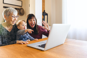 Wall Mural - Cheerful multigenerational family video calling through laptop in living room at home