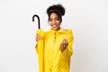 Wall Mural - Young woman with rainproof coat and umbrella isolated on white background inviting to come with hand. Happy that you came