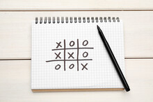 Notebook With Tic Tac Toe Game And Marker On White Wooden Table, Top View