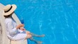 © Евгения Медведева - relaxing senior woman dangling her legs in an outdoor swimming pool holding a blue refreshing cocktail wearing a straw hat. Summer rest. All inclusive
