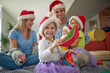 © luckybusiness - A young family with christmas caps is sitting on the floor and posing for a photo together during christmas holidays at home. Christmas, home, family