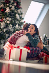 Wall Mural - A young couple in love is in a hug while sitting on the floor at home and sharing christmas presents. Christmas, home, relationship, presents