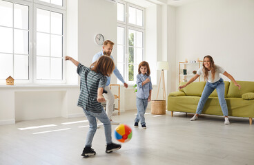 Wall Mural - Happy family playing ball inside the house. Young mother, father and little children playing football with a toy ball at home. Mommy, daddy and kids playing soccer and having lots of fun together