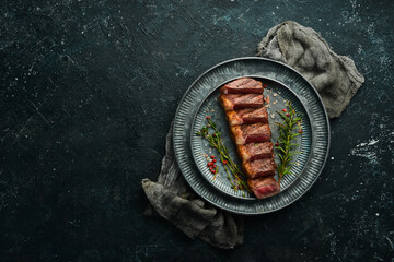 Wall Mural - grilled marbled beef steaks striploin with spices. On a black stone background.