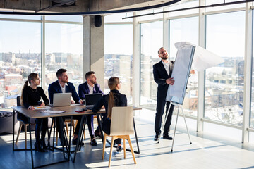 The boss stands near the board with graphs, demonstrates statistics, various personnel attending the training, introduces the new products of the company, reports on the results of work for partners.